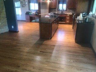 Hardwood kitchen floor with a dark island, wooden cabinets, and windows.