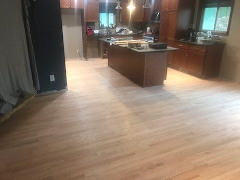 Light wood flooring in a kitchen with a dark island and cabinets. Window in the background.