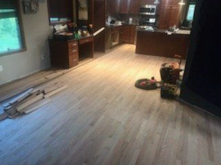 Light wood flooring in a home's kitchen and dining area; wooden boards stacked nearby, unfinished.