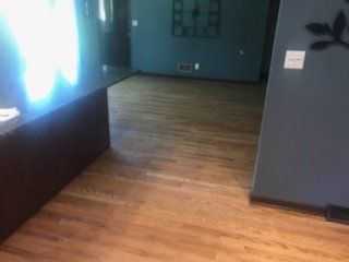 Hardwood floor in room with blue walls, part of a dark counter visible.