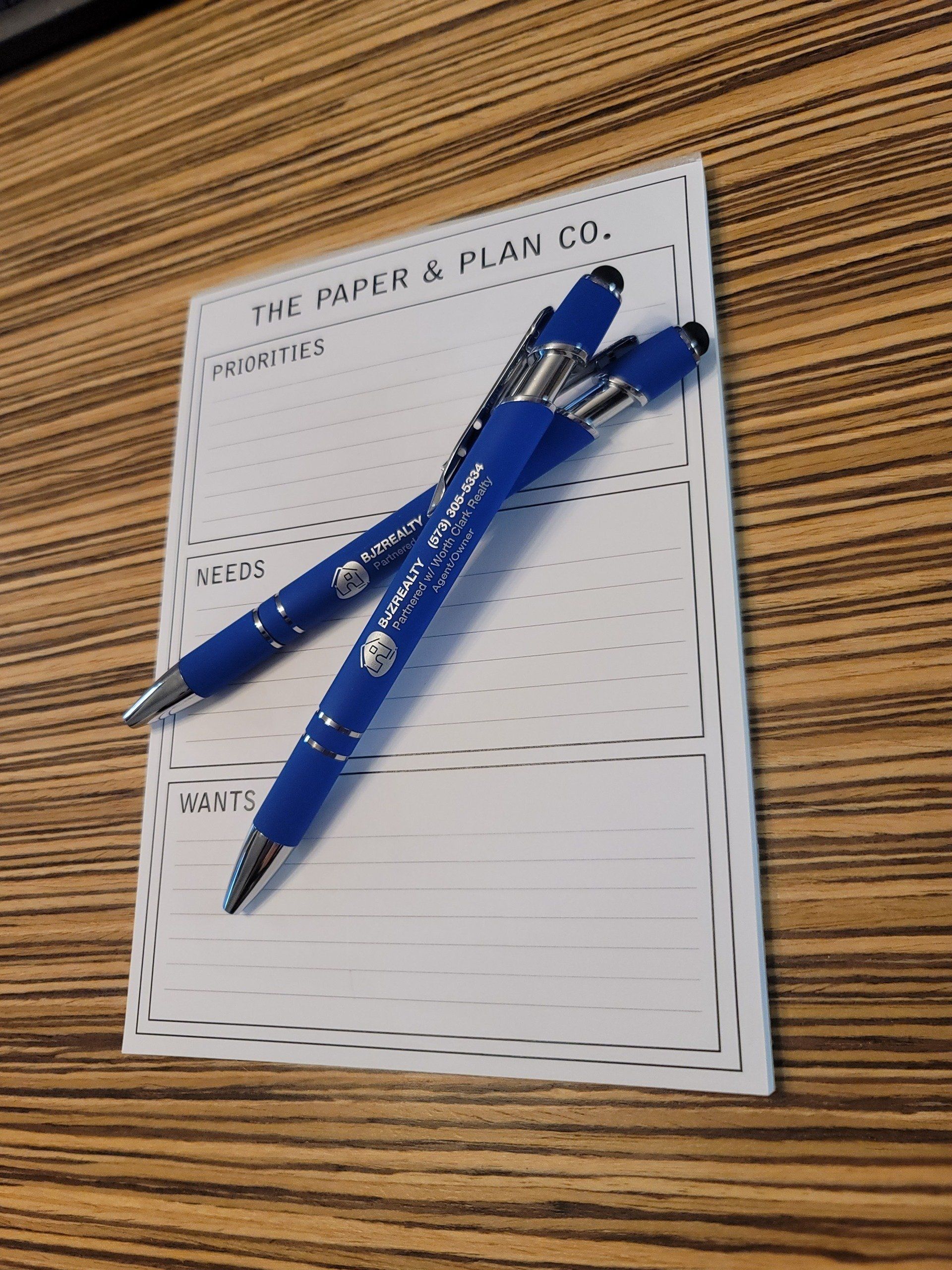 Two blue pens are sitting on top of a notepad that says the paper & plan co.