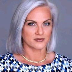 A woman with gray hair is wearing a blue and white dress and a necklace.