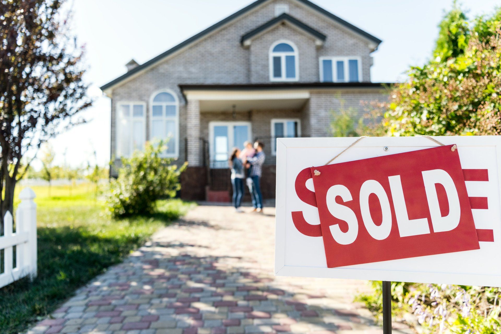 A couple standing in front of a house with a sold sign in front of it.