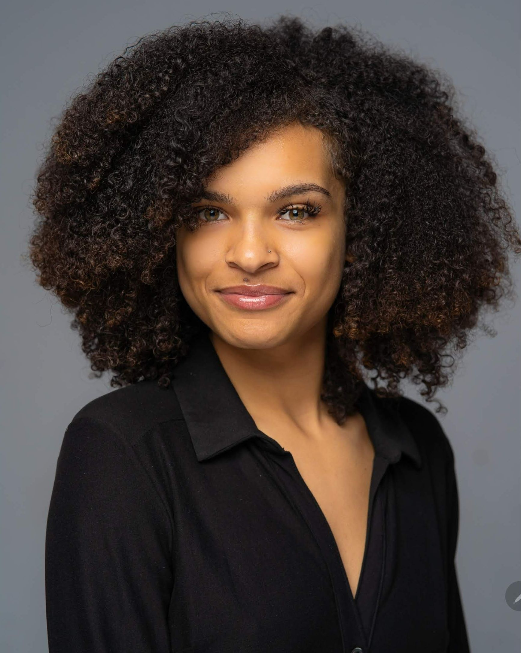 A woman with curly hair is wearing a black shirt and smiling.