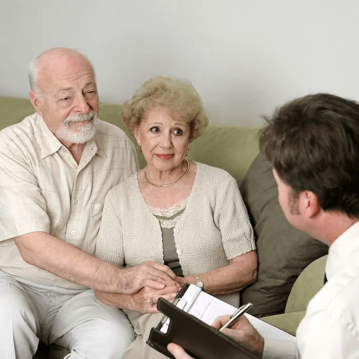 An elderly couple sitting on a couch talking to a man holding a clipboard