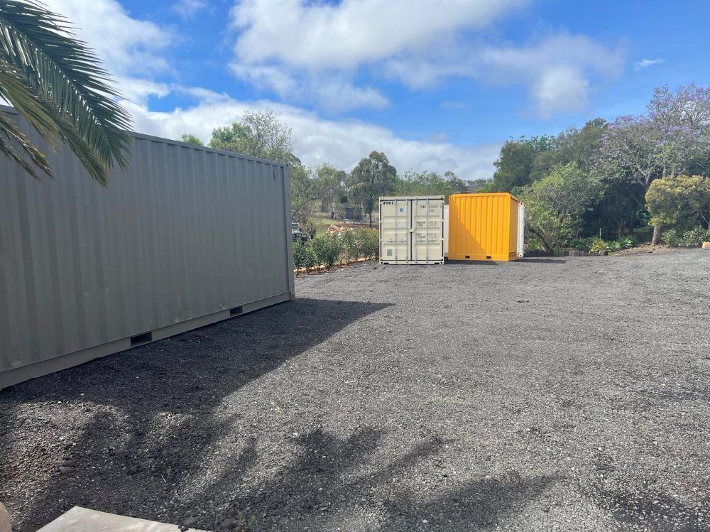 Two Shipping Containers Are Parked in a Gravel Lot Next to a Palm Tree — Toowoomba Container Hire & Sales in Oakey, QLD