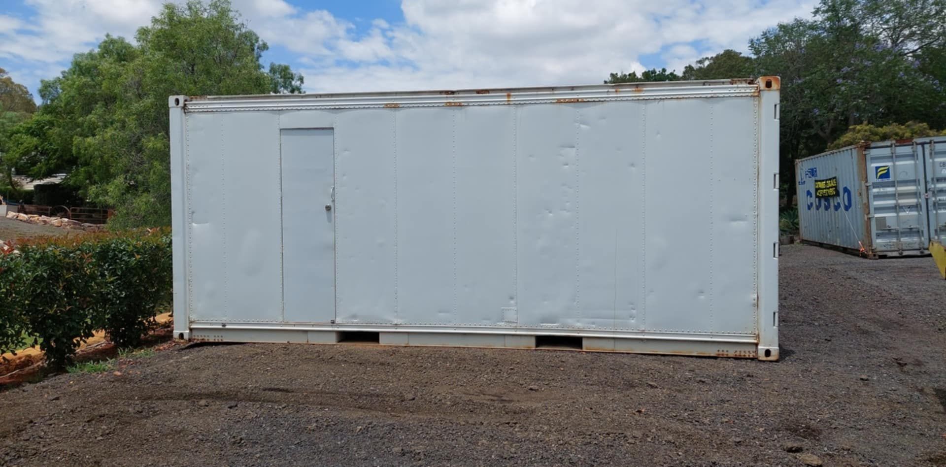 A wHite Shipping Container With a Door is Sitting in a Gravel Lot — Toowoomba Container Hire & Sales in Oakey, QLD