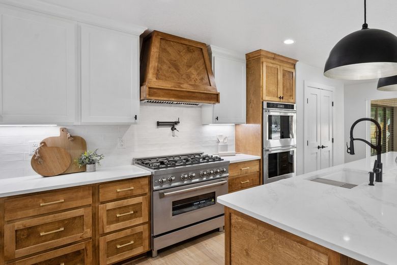 A modern kitchen featuring white cabinets, wood lower cabinets, a herringbone wood vent hood, and stainless steel appliances.