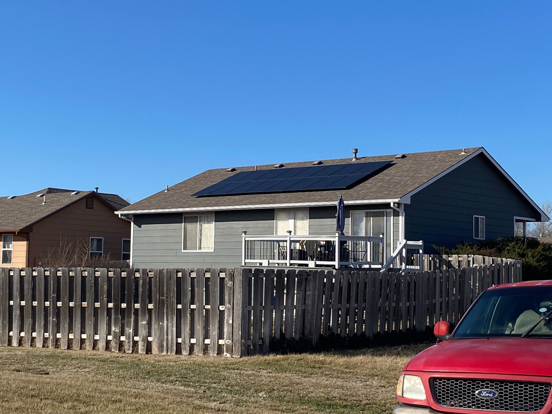 A red truck is parked in front of a house with solar panels on the roof.