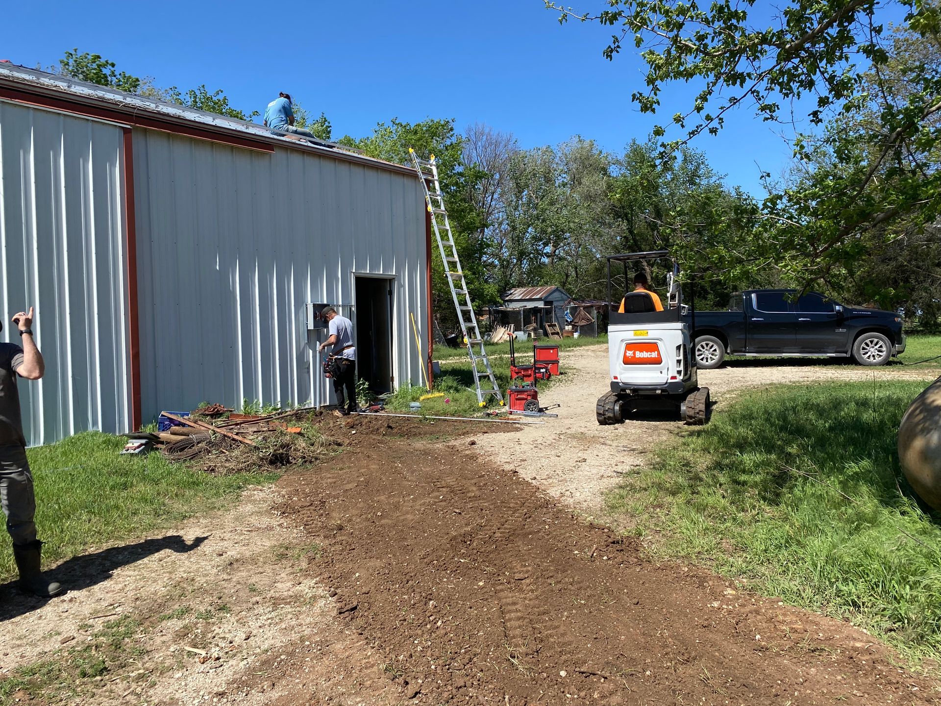 A man is standing on a dirt road in front of a building.