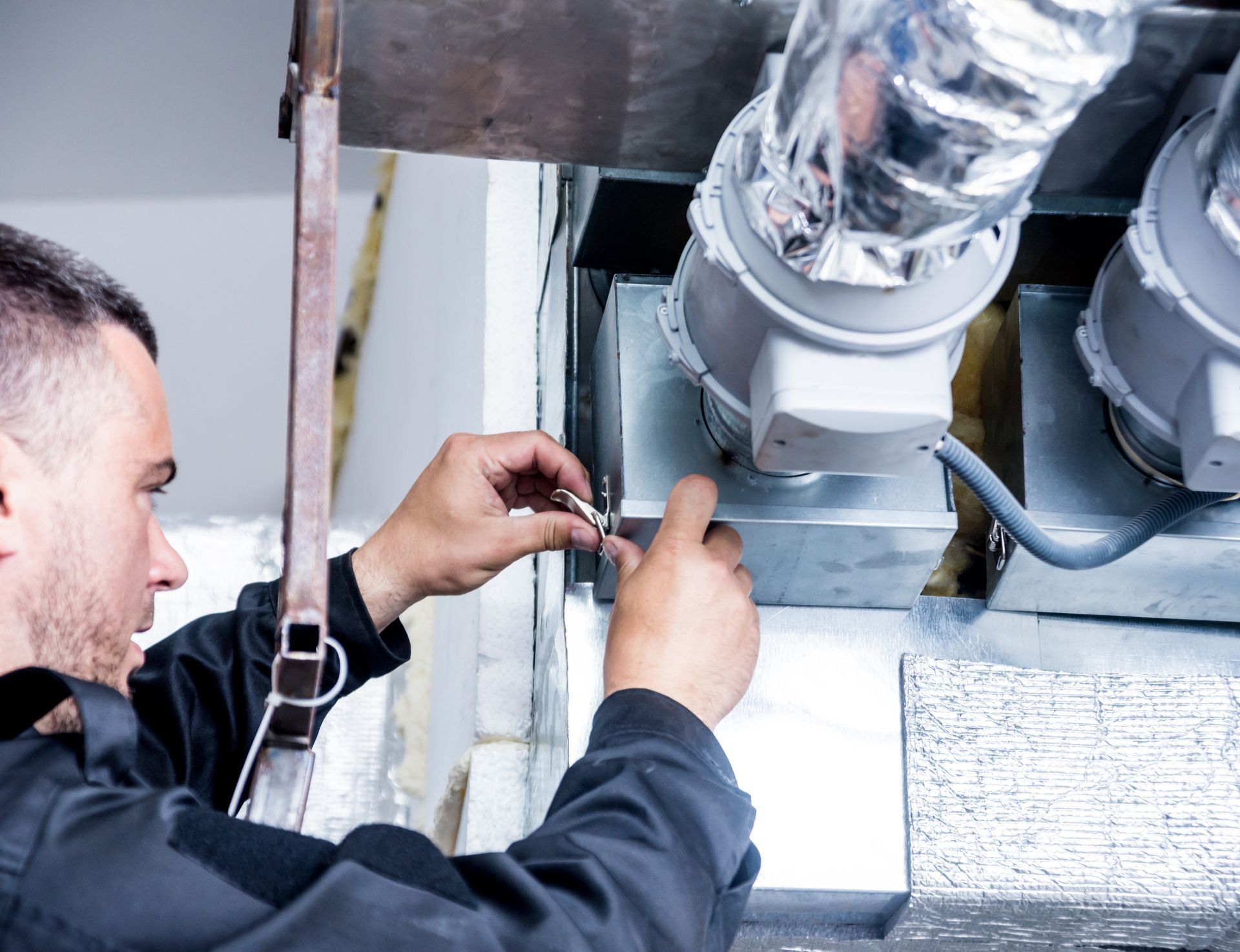 A man is working on a ventilation system in a building.