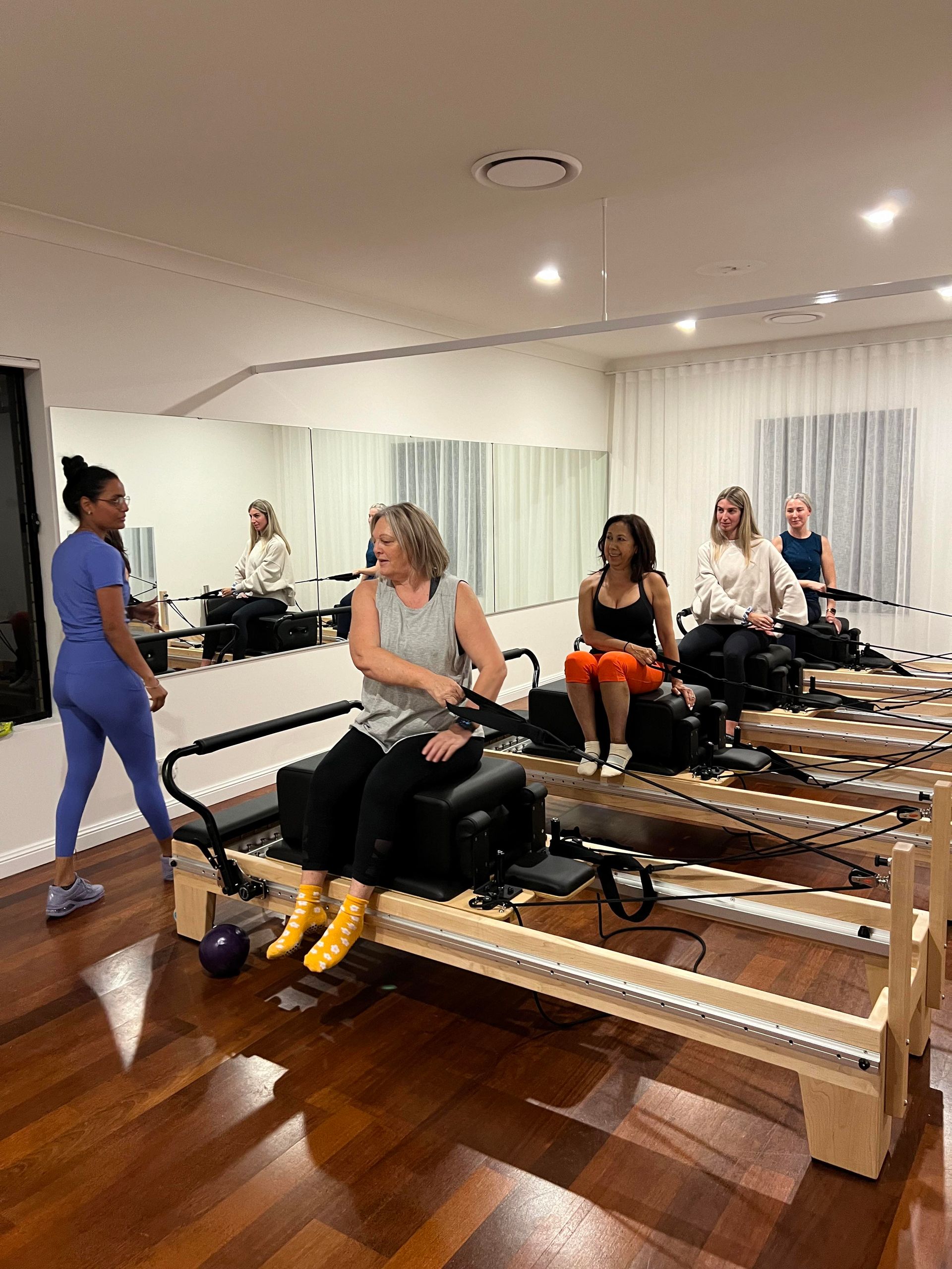 A group of women are sitting on pilates machines in a treatment room.