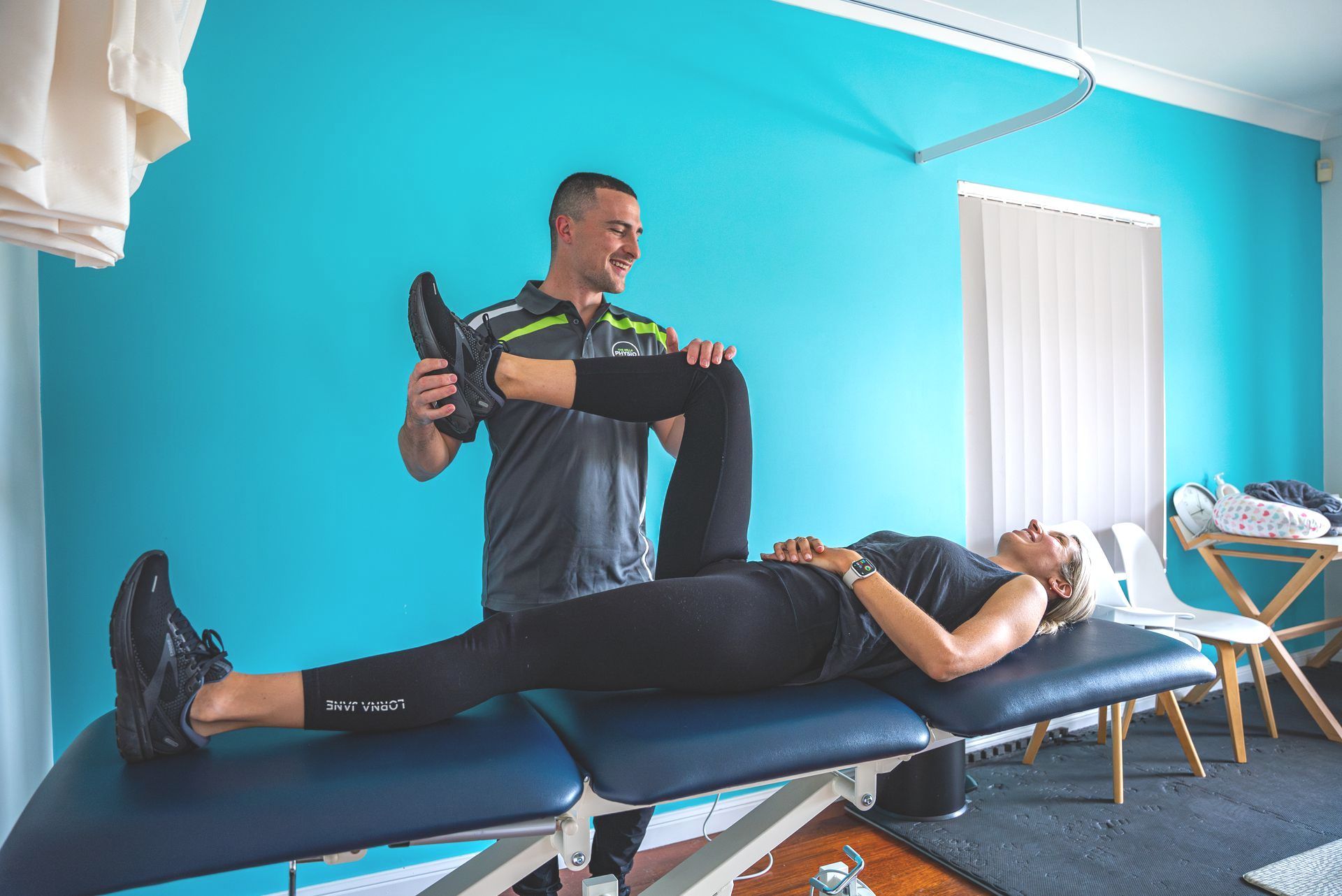 Cyclist sitting on bed with hips being assessed by male physio