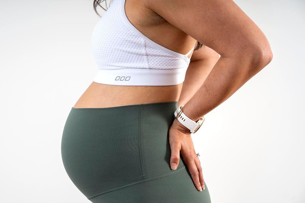 close up of pregnant person's belly, with their hands support their lower back
