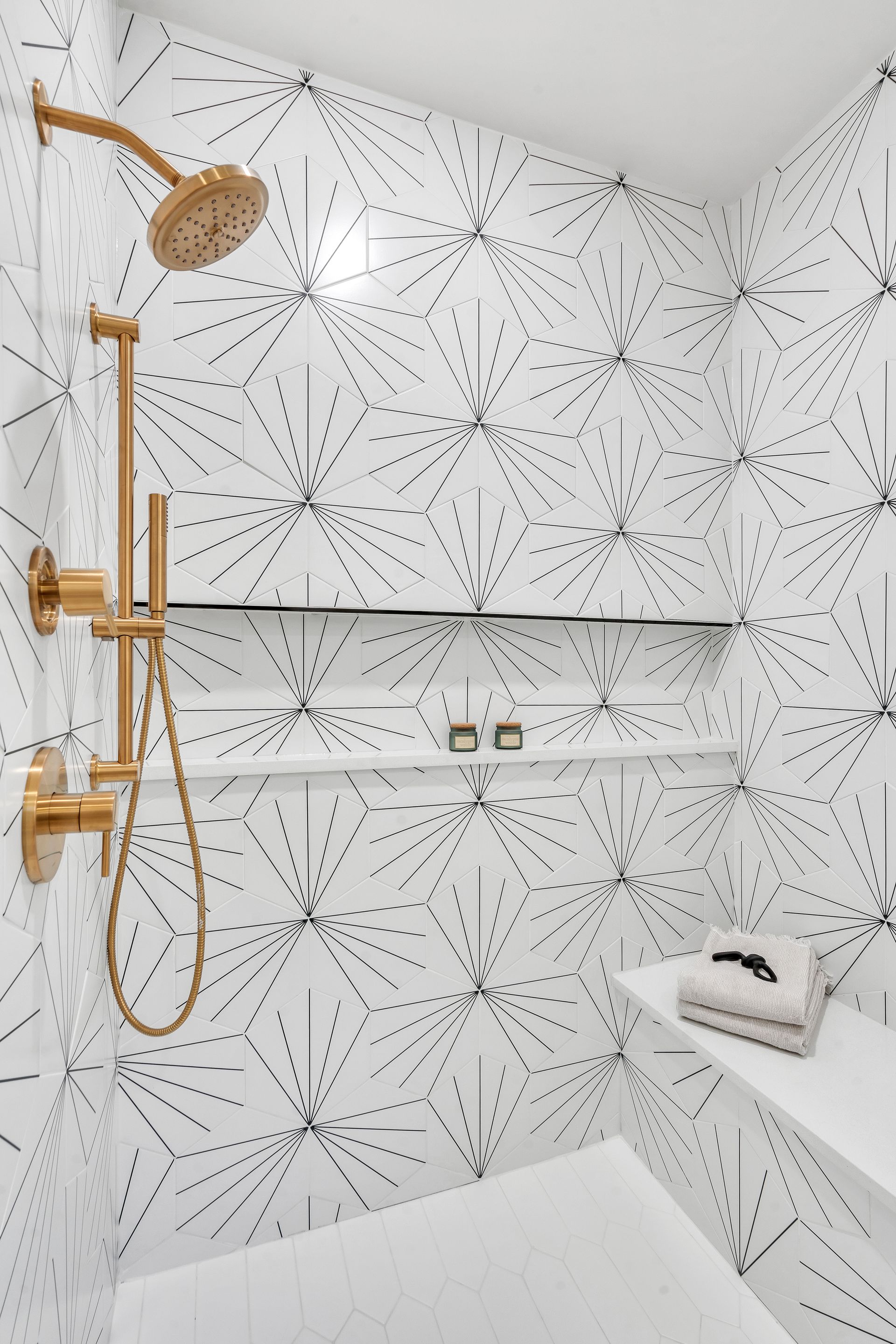 Gold shower fixtures against white geometric tile in a modern bathroom.