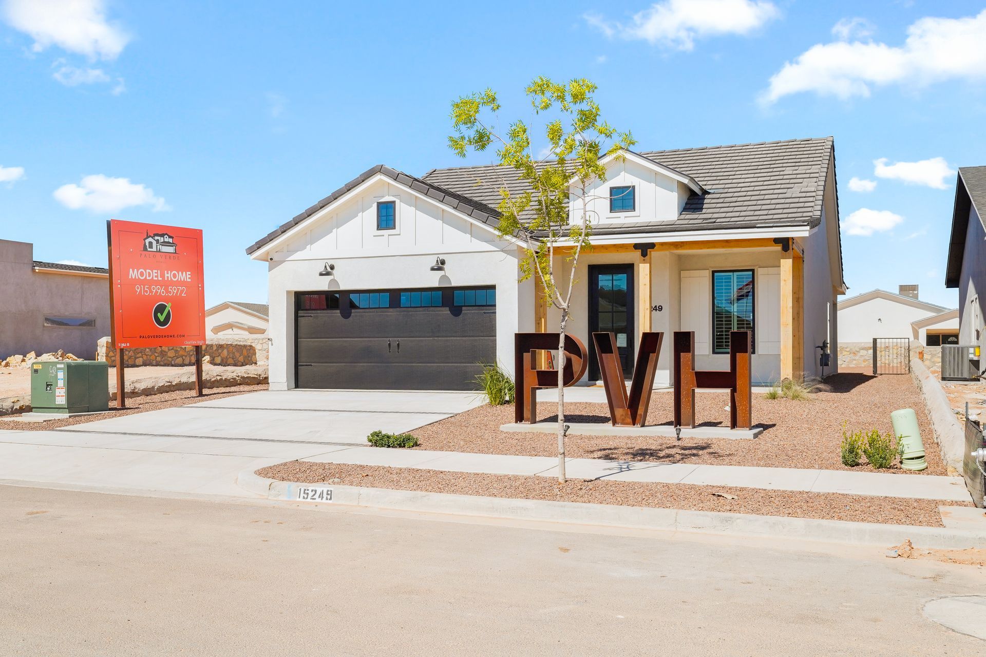 White farmhouse-style house with brown garage door, and a sign in a sunny setting.