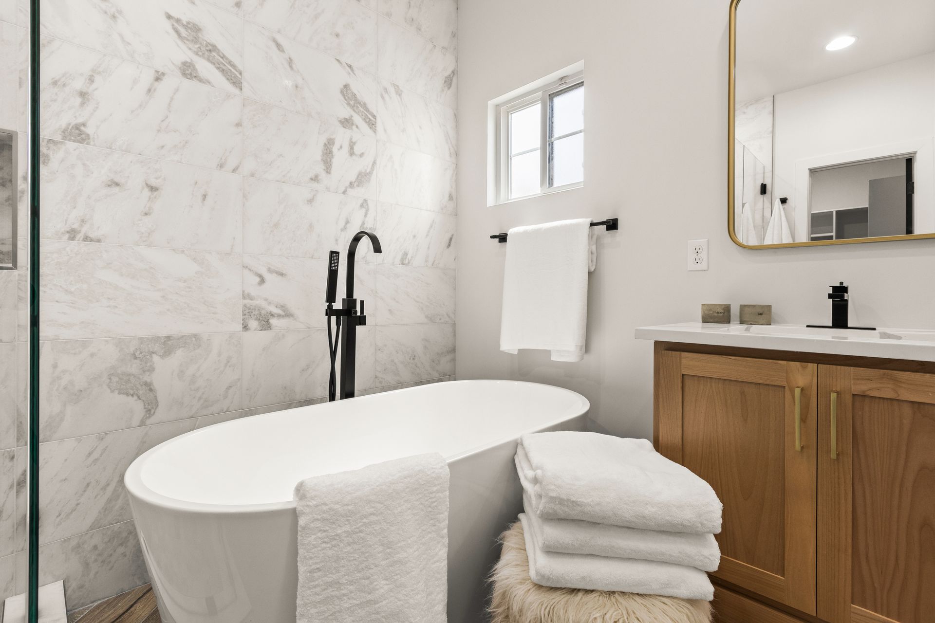 Bathroom with white soaking tub, marble tile, and wooden vanity.