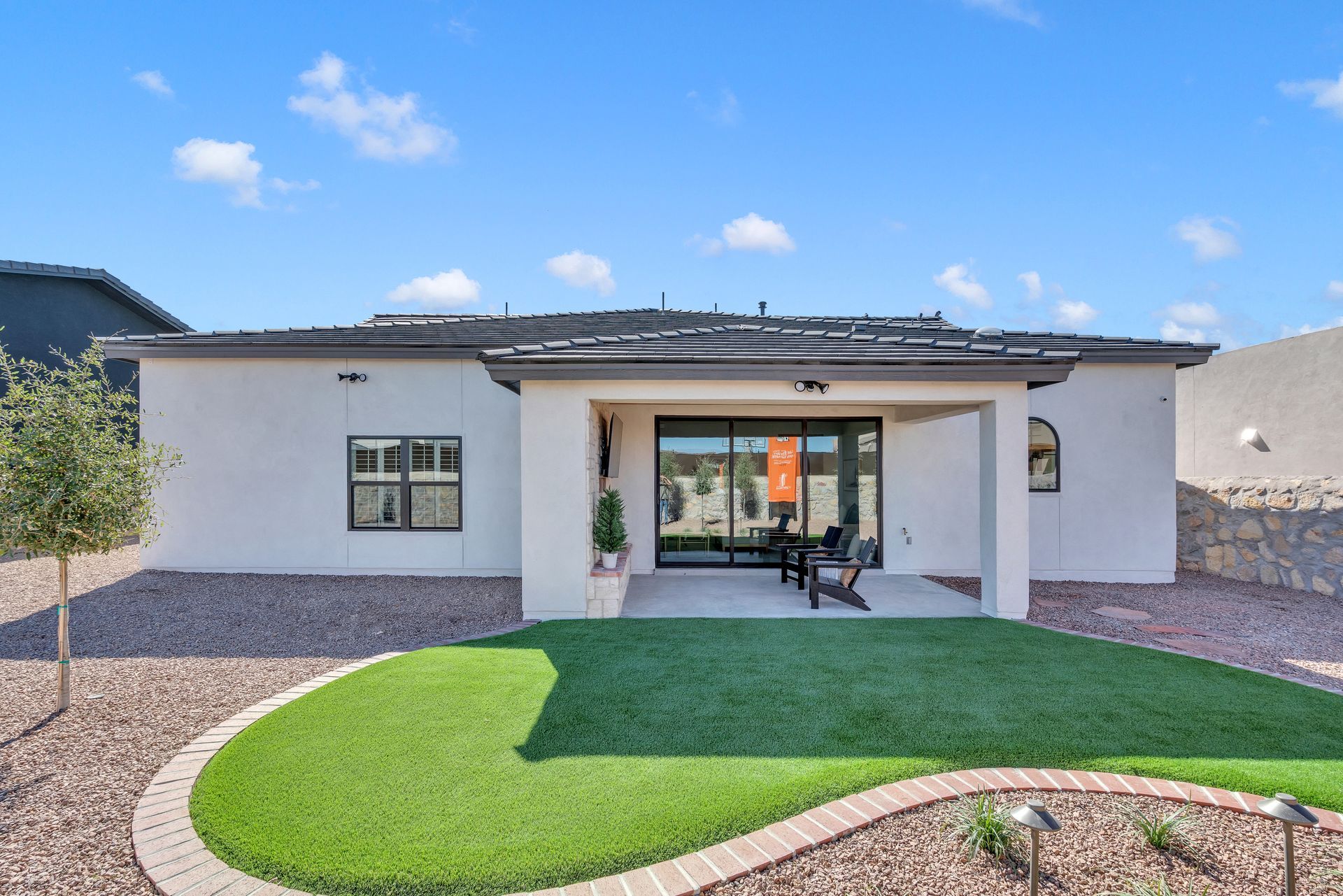 Back of a white house with a covered patio, green lawn, and gravel landscaping under a blue sky.