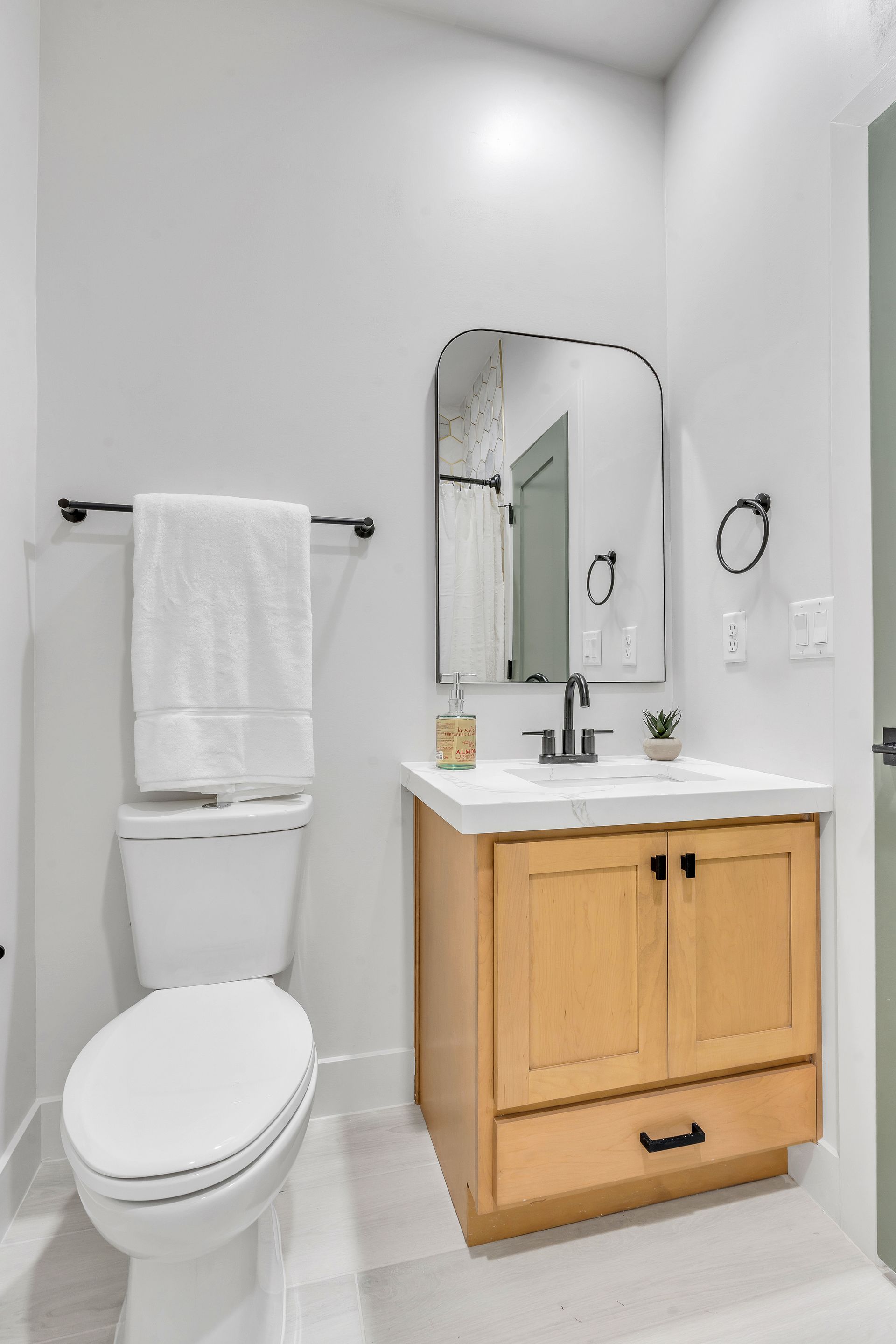 Bathroom with toilet, vanity with mirror, and towel rack; light wood and white fixtures.