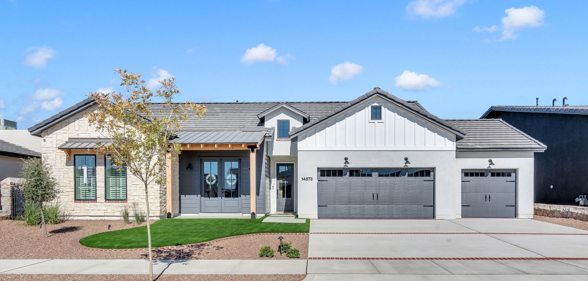 A modern single-story home with light-colored exterior, gray garage doors, and blue sky.