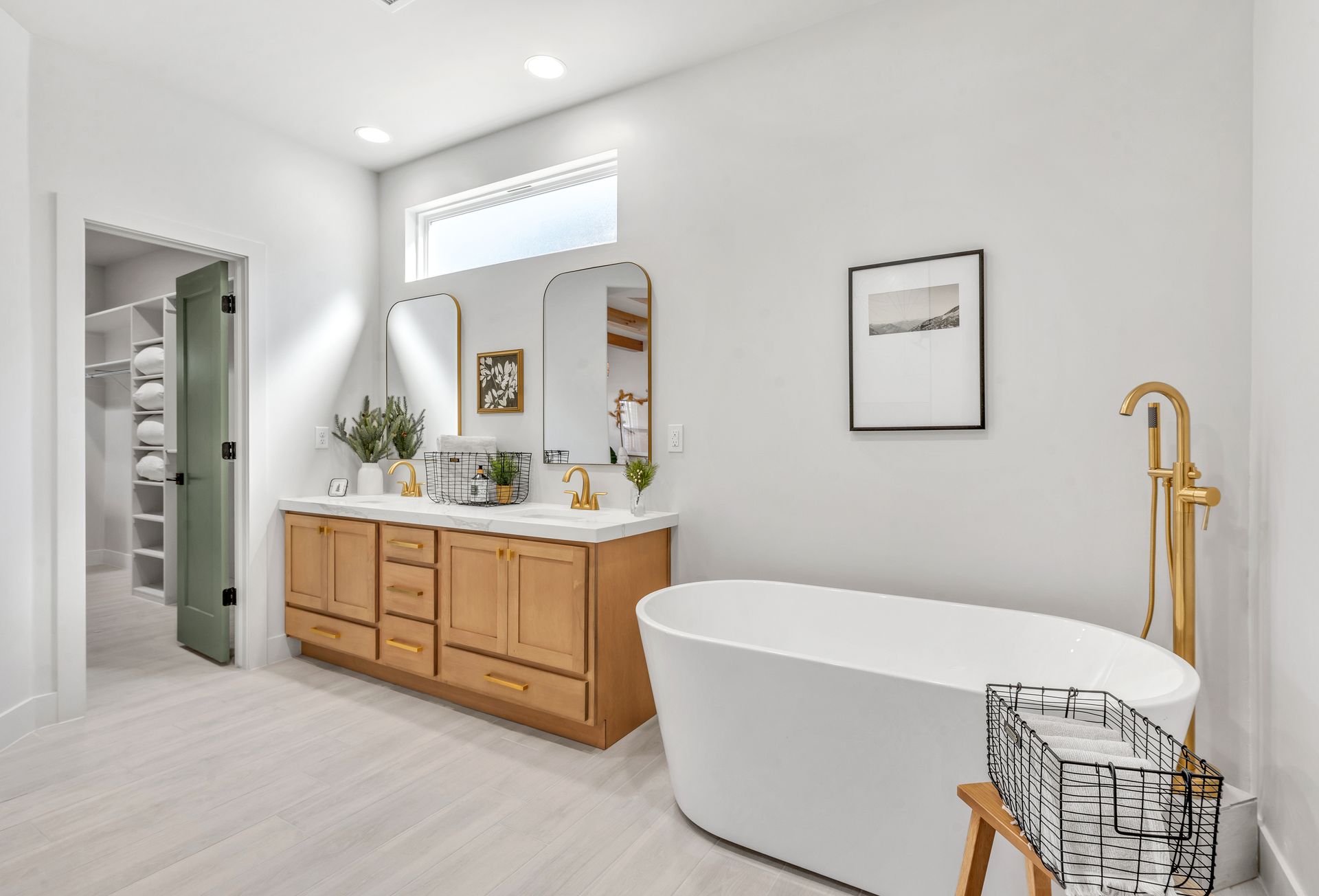 Modern bathroom with a light wood vanity, white tub, and gold fixtures.