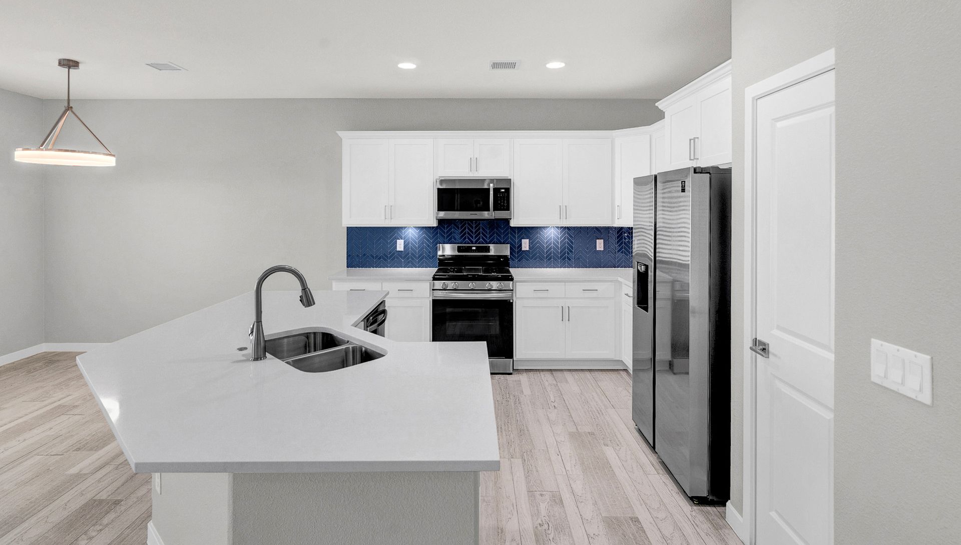 Modern kitchen with white cabinets, blue backsplash, and stainless steel appliances.