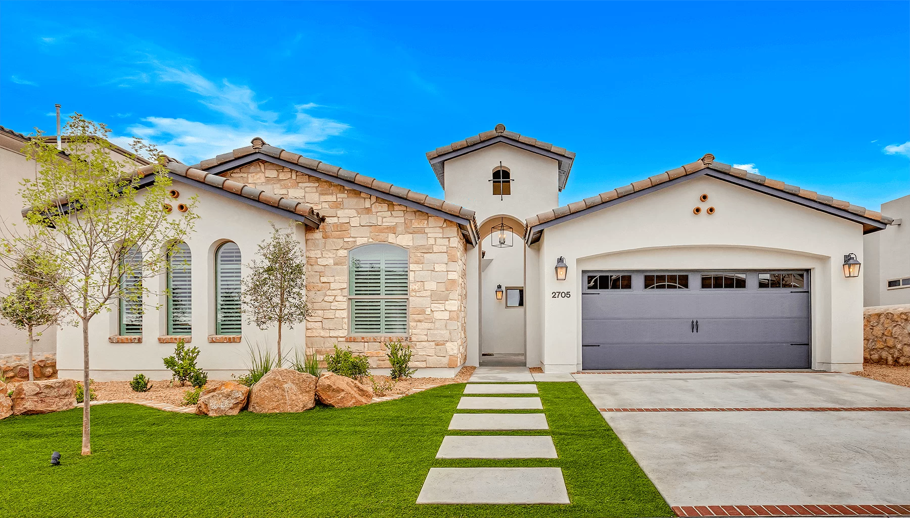 Beige stucco home with stone accents, gray garage door, and a blue sky.