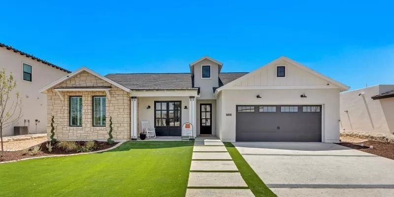 Modern white house with a stone facade, black door, and green lawn. Gray garage door and clear sky.