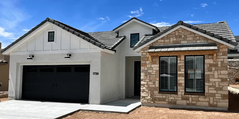 A modern home with white stucco, stone accents, and a black garage door under a blue sky.