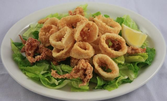 Fried calamari rings on a bed of lettuce with a lemon wedge on a white plate.