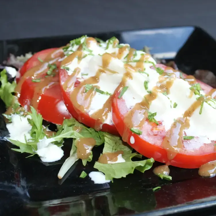 Tomato and mozzarella salad with drizzled sauce and herbs on a bed of lettuce.
