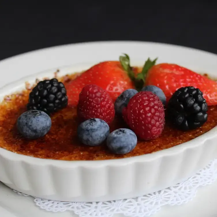 Crème brûlée in a white dish topped with fresh berries.