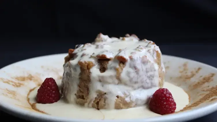 Bread pudding with cream sauce and raspberries on a white plate.