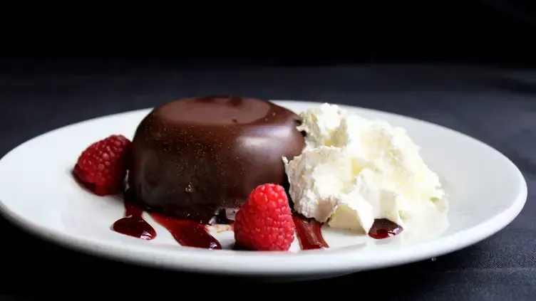 Chocolate dessert with whipped cream and raspberries on a white plate.