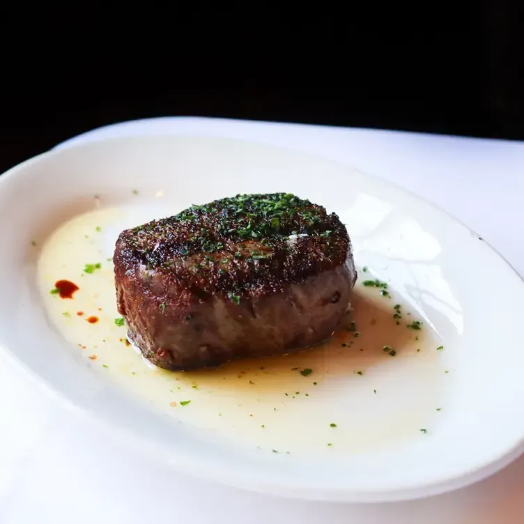 Grilled steak on a white plate with a buttery sauce, garnished with herbs.