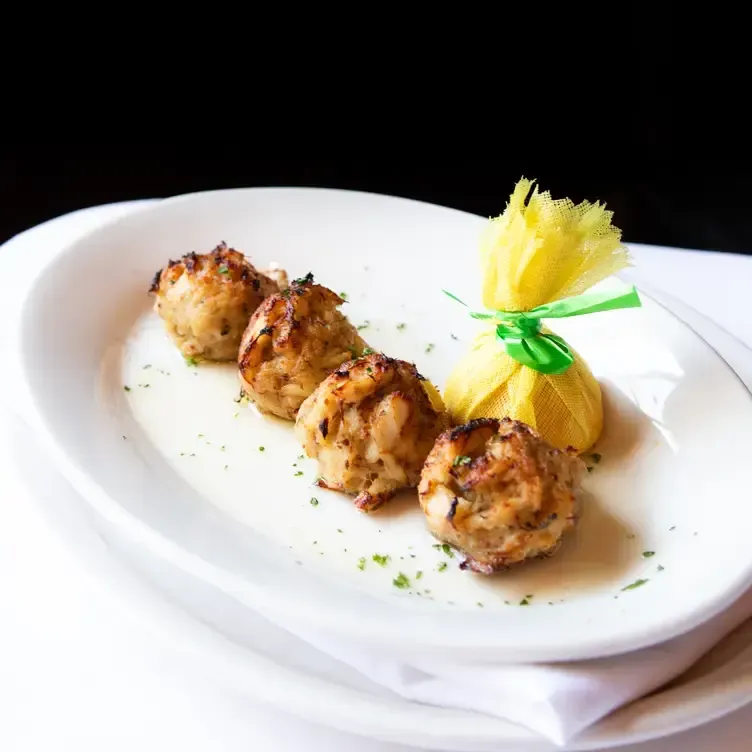 Four crab cakes and a lemon pouch on a white plate, with a black background.