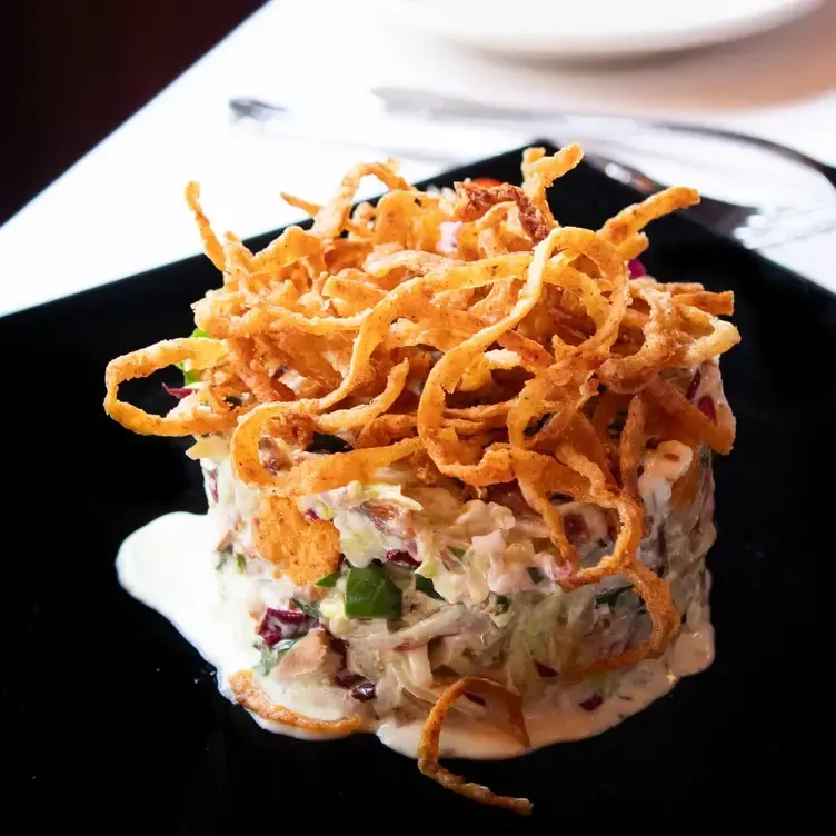 Salad with fried onion topping on a black plate, white sauce.