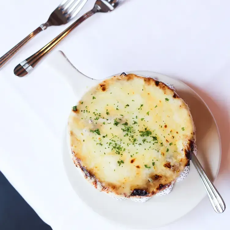 French onion soup in a white bowl, covered in melted cheese, with two forks and a spoon.