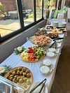 Buffet table with various appetizers, including vegetables and dips, set near a window.