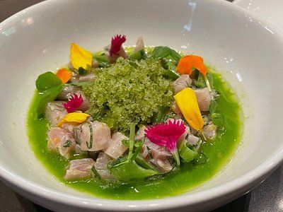 Ceviche in a white bowl, with diced fish in green sauce, garnished with flowers and green granules.