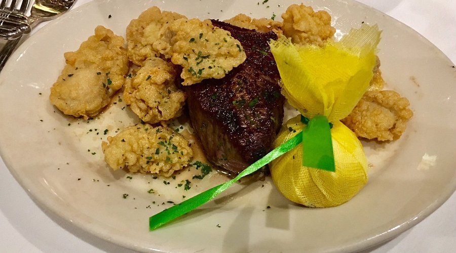 Steak and fried food on a white plate, garnished with lemon and parsley.