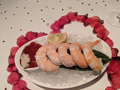 Shrimp cocktail on ice, with a lemon wedge and dipping sauce, decorated with rose petals.