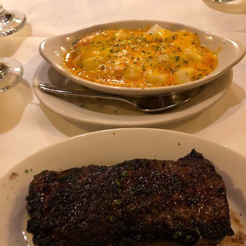 Steak and mac and cheese on plates, set on a white tablecloth.