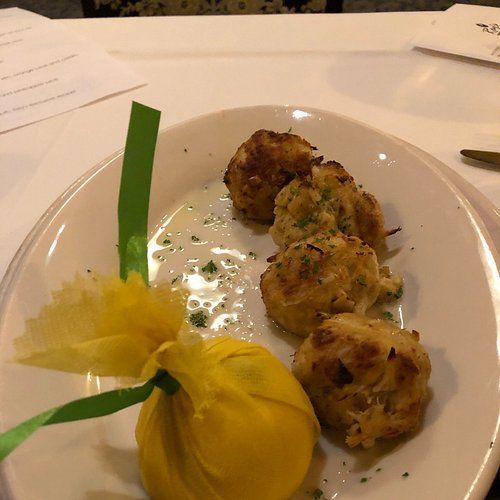 Appetizer plate with four crab cakes and a lemon wrapped in yellow tulle.