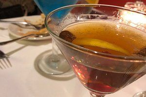 Close-up of a cocktail in a martini glass with a lemon slice and cinnamon stick.