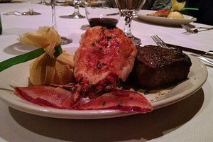 Plate of surf and turf: lobster tail, steak, corn, on a white plate.