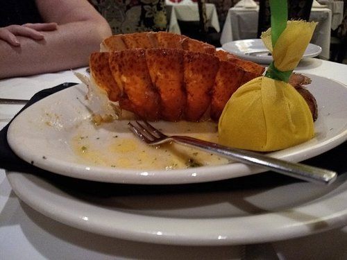 Lobster tail on a white plate with a lemon wedge; person at table.
