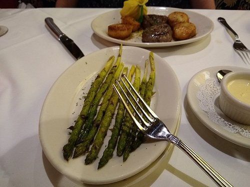 Plate of asparagus with fork; steak and scallops in background, white tablecloth.