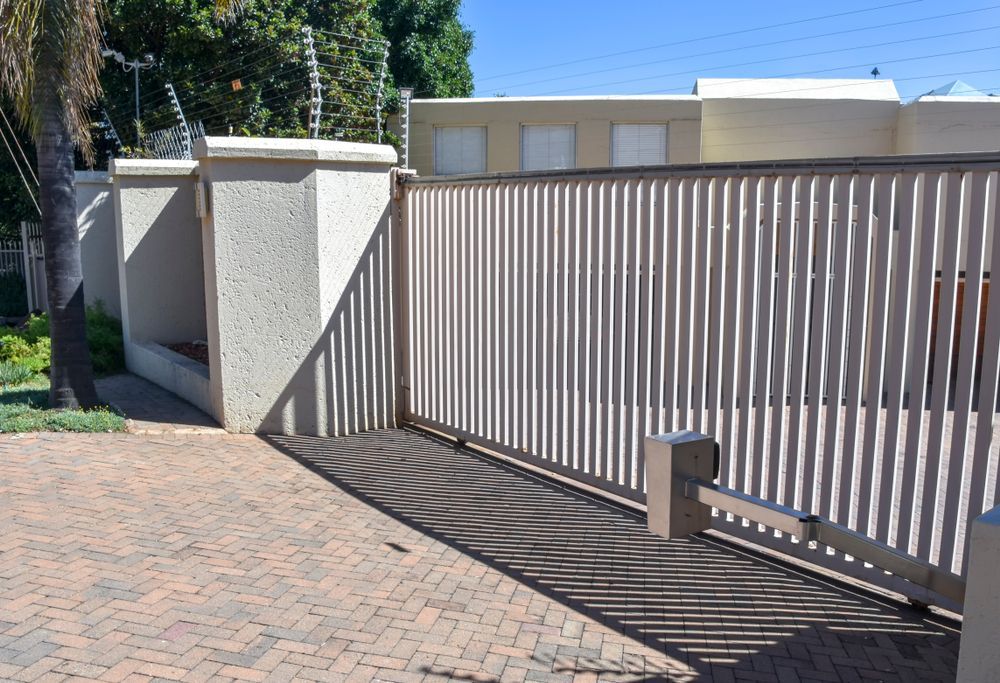 A Beige Metal Sliding Gate Stands Closed Against a Stucco Wall — A Betta Fence 'N' Yard In Lake Cathie, NSW