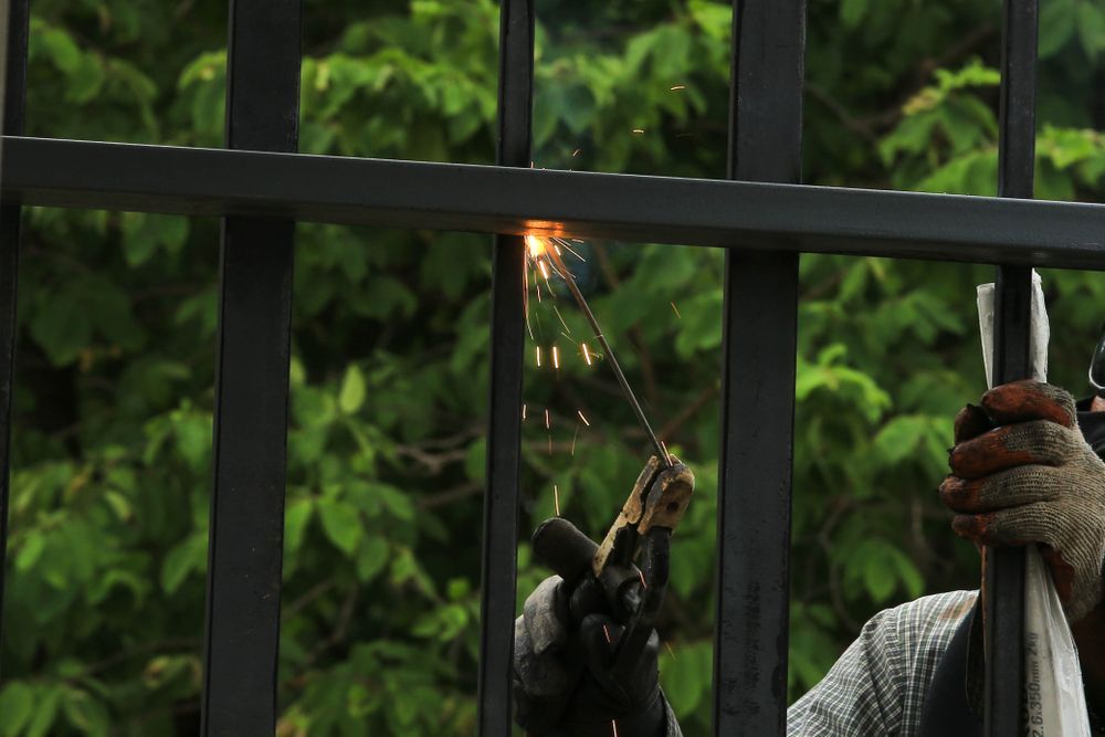 A Person Wearing Work Gloves Welds a Black Metal Fence — A Betta Fence 'N' Yard In Wauchope, NSW